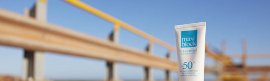 Maxiblock Essential SPF 50+ sunscreen tube on an Australian worksite with steel framework and clear sky behind it