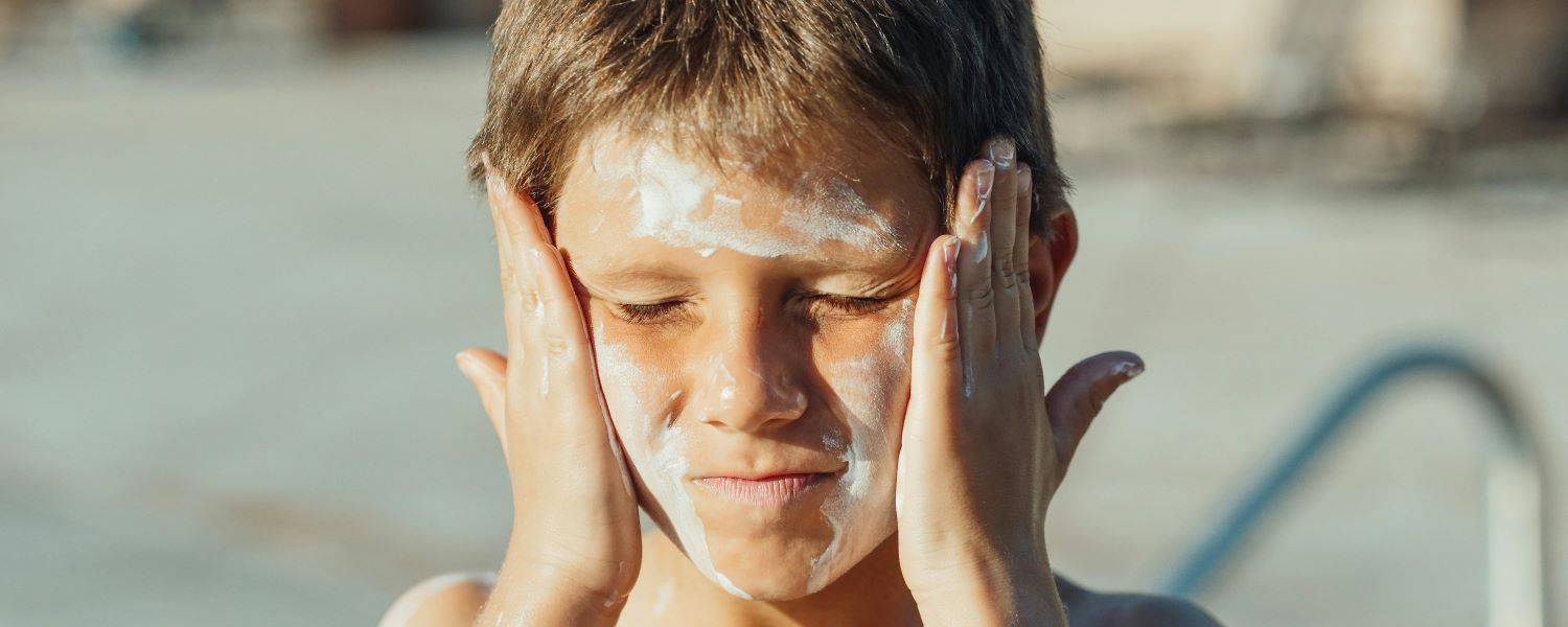 a frustrated boy applying sunscreen on his face
