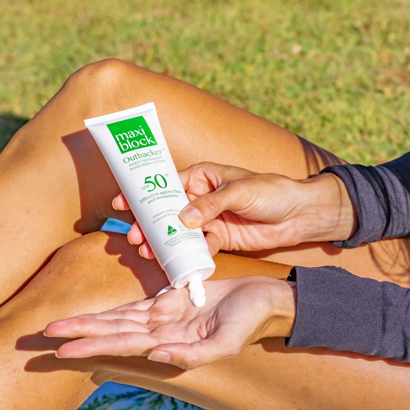 Person applying Maxiblock Outbacker Sunscreen With Insect Repellent SPF 50+ 100g to their hand with grass in the background