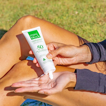 Person applying Maxiblock Outbacker Sunscreen With Insect Repellent SPF 50+ 100g to their hand with grass in the background