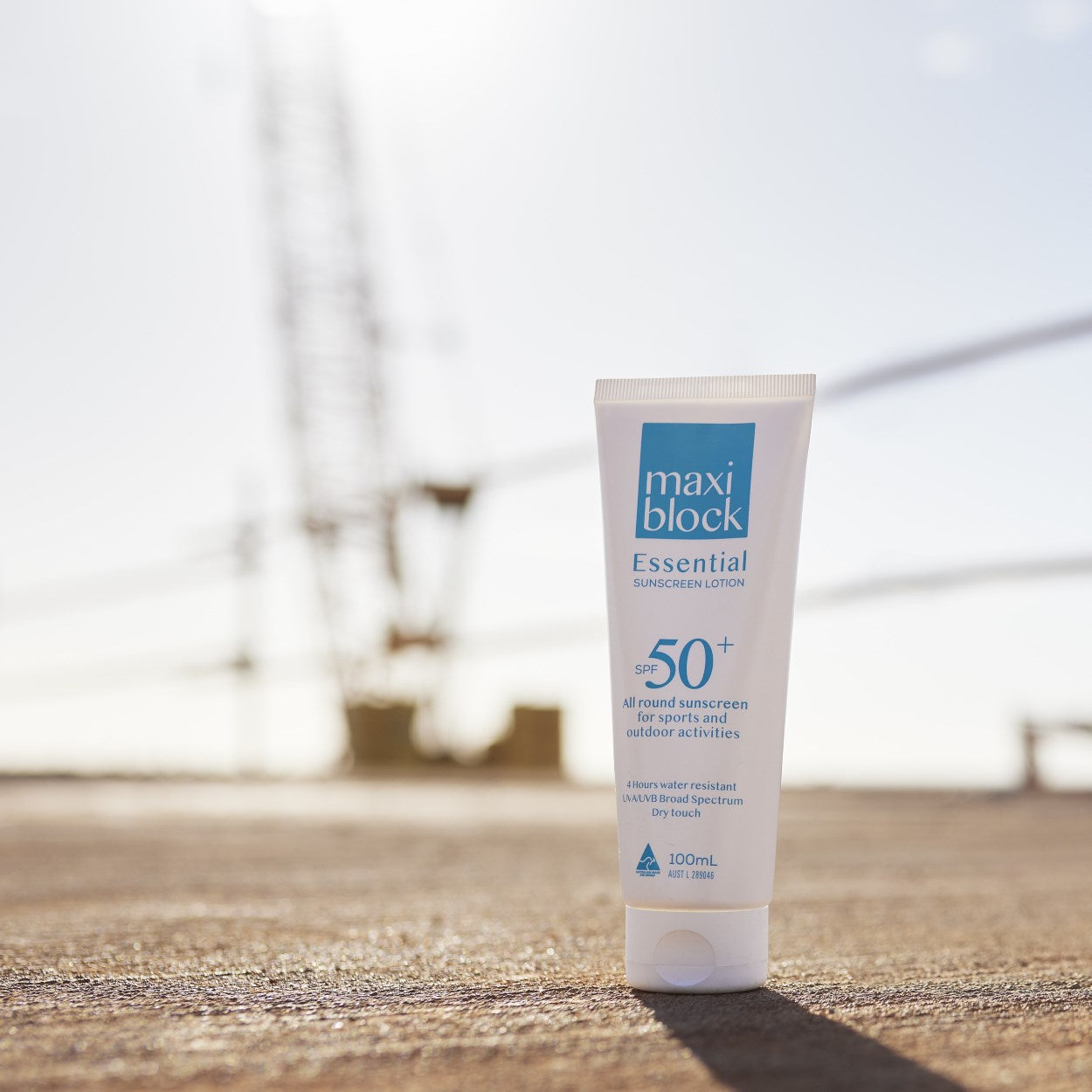 Maxiblock Essential SPF 50+ 100mL tube on a concrete rooftop with crane in background