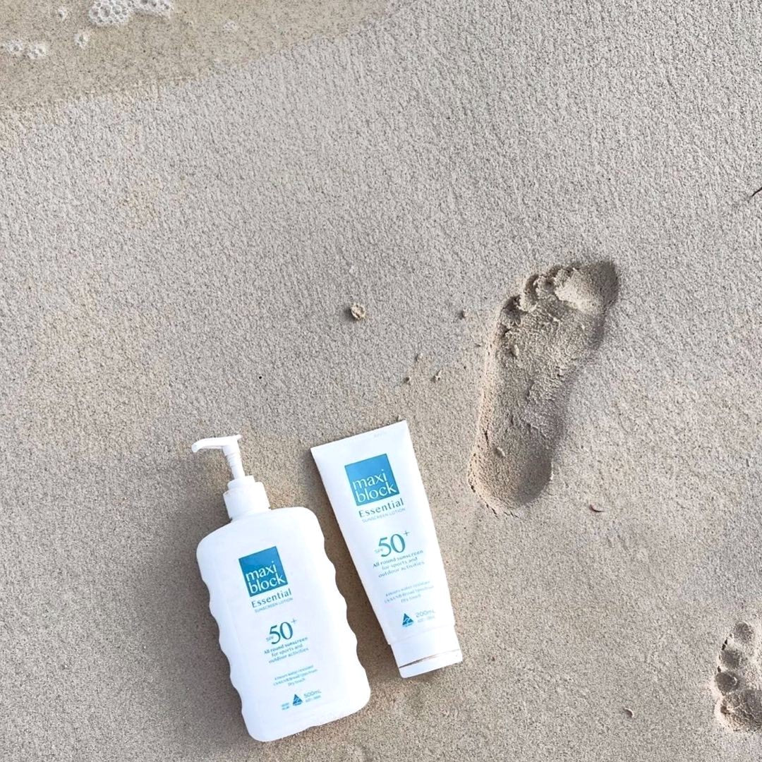 Maxiblock Essential sunscreen bottle and tube on sand beside a footprint at an Australian beach
