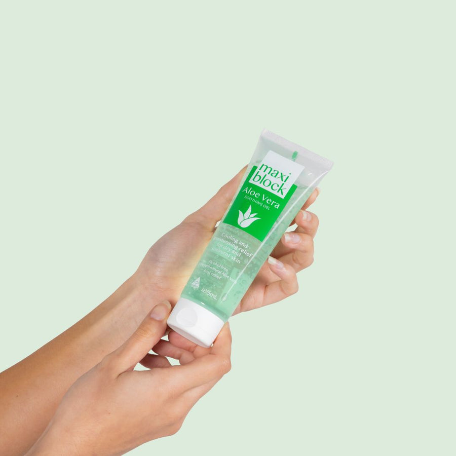 Hand holding Maxiblock Aloe Vera Gel 125mL tube against a green background.