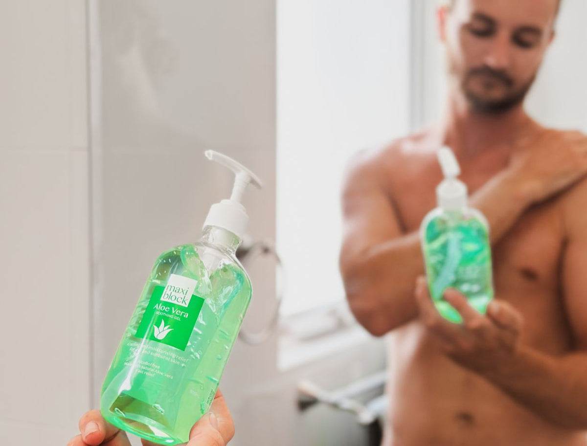 Maxiblock Aloe Vera Gel 500mL pump bottle held up in a bathroom, with a man applying gel to his arm in the background.